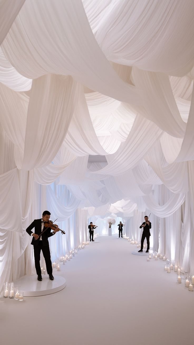 A candlelit white-draped event corridor with live string musicians